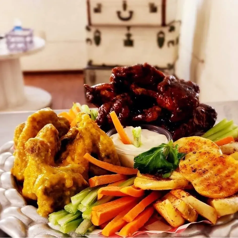 Alitas de pollo con dos salsas, una BBQ y otra miel, acompañadas de papas asadas y vegetales.