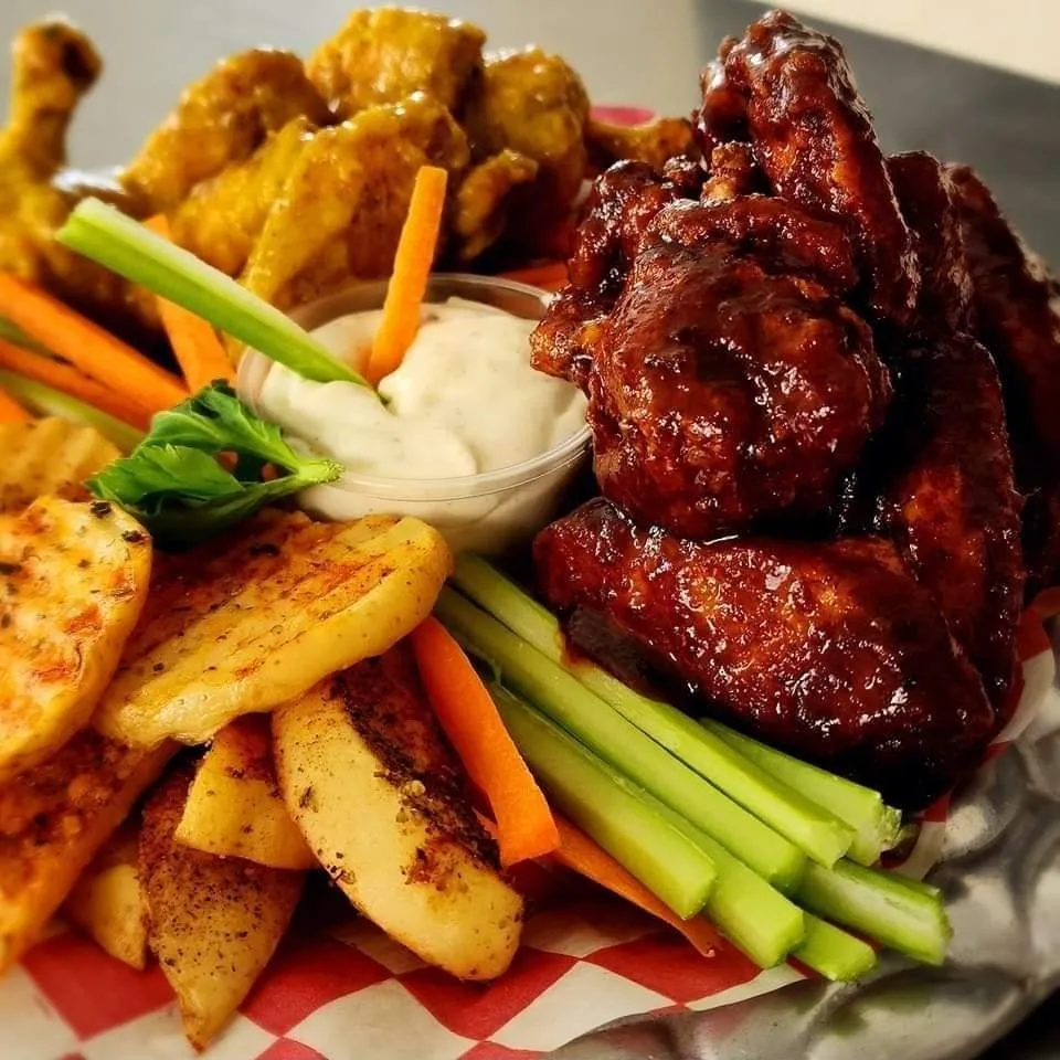 Plato irresistible de alitas de pollo con una variedad de salsas, papas y vegetales.