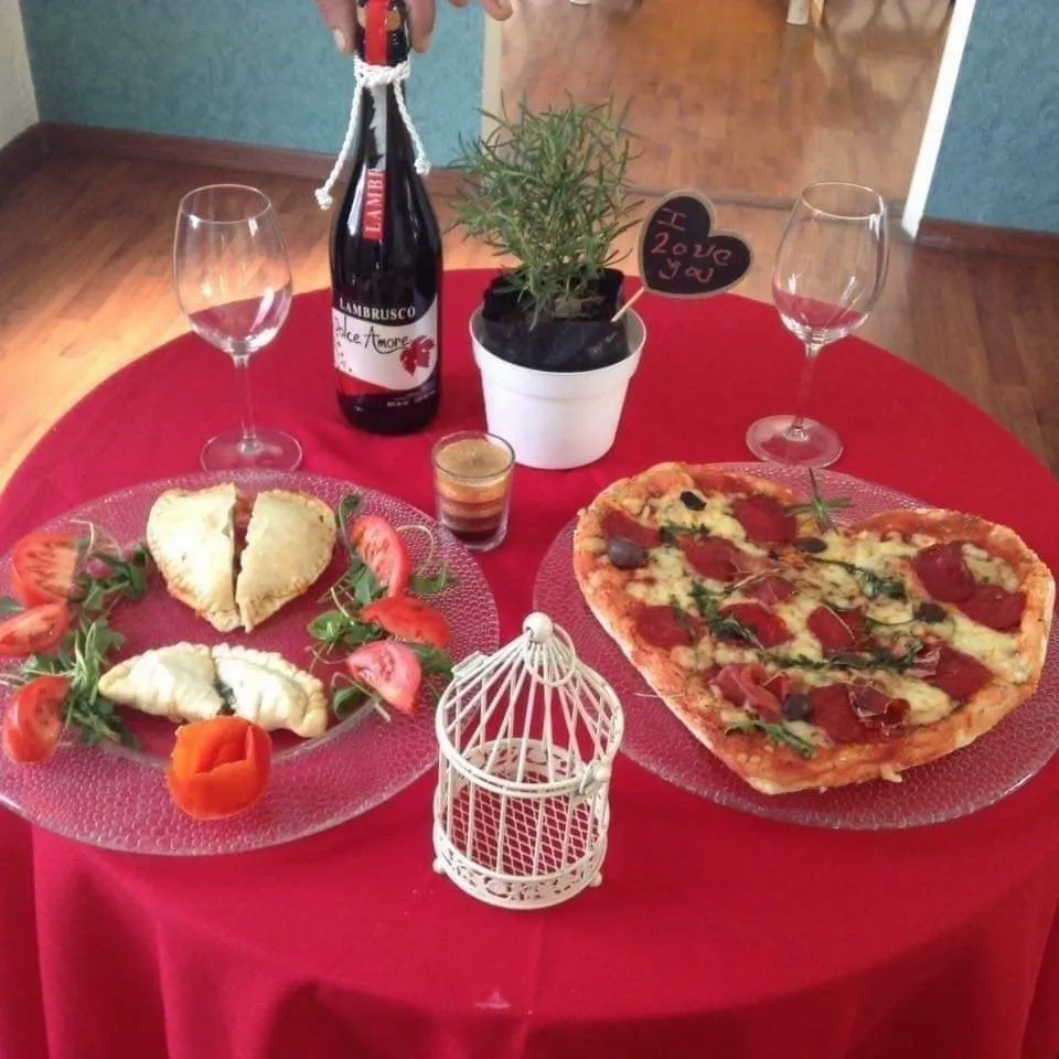 Imagen de una mesa romántica con pizza en forma de corazón, empanadas y vino. Celebrando el amor con pizza, empanadas y buen vino.