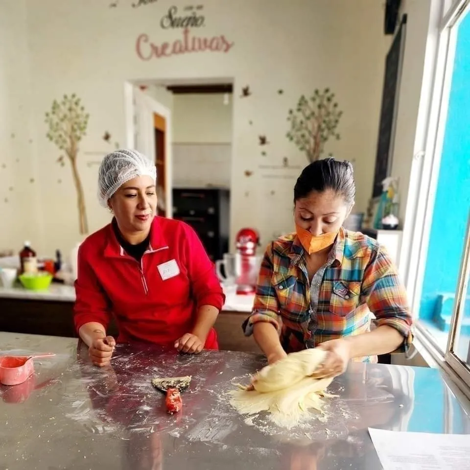 Mujeres horneando una rosca de reyes en una clase de cocina.