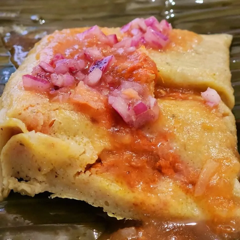 Imagen de tamales recién hechos, con salsa y cebolla.
